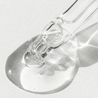 Close-up of a clear glass bottle with a dropper on a light gray background