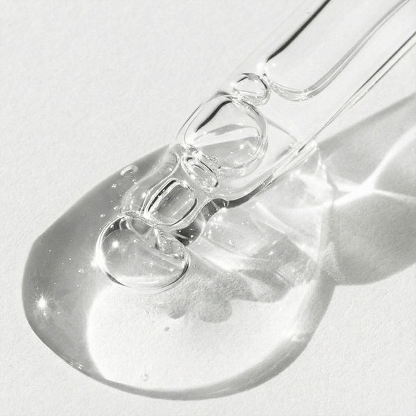 Close-up of a clear glass bottle with a dropper on a light gray background