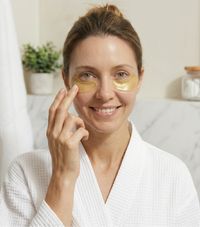 Woman wearing gold eye patches in a bathroom setting