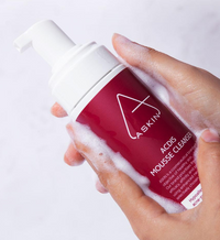 Hand holding a red and white bottle of A-SKIN ACDS Mousse Cleanser with foam.