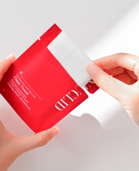 Red and white skincare product packaging held by a hand against a light background